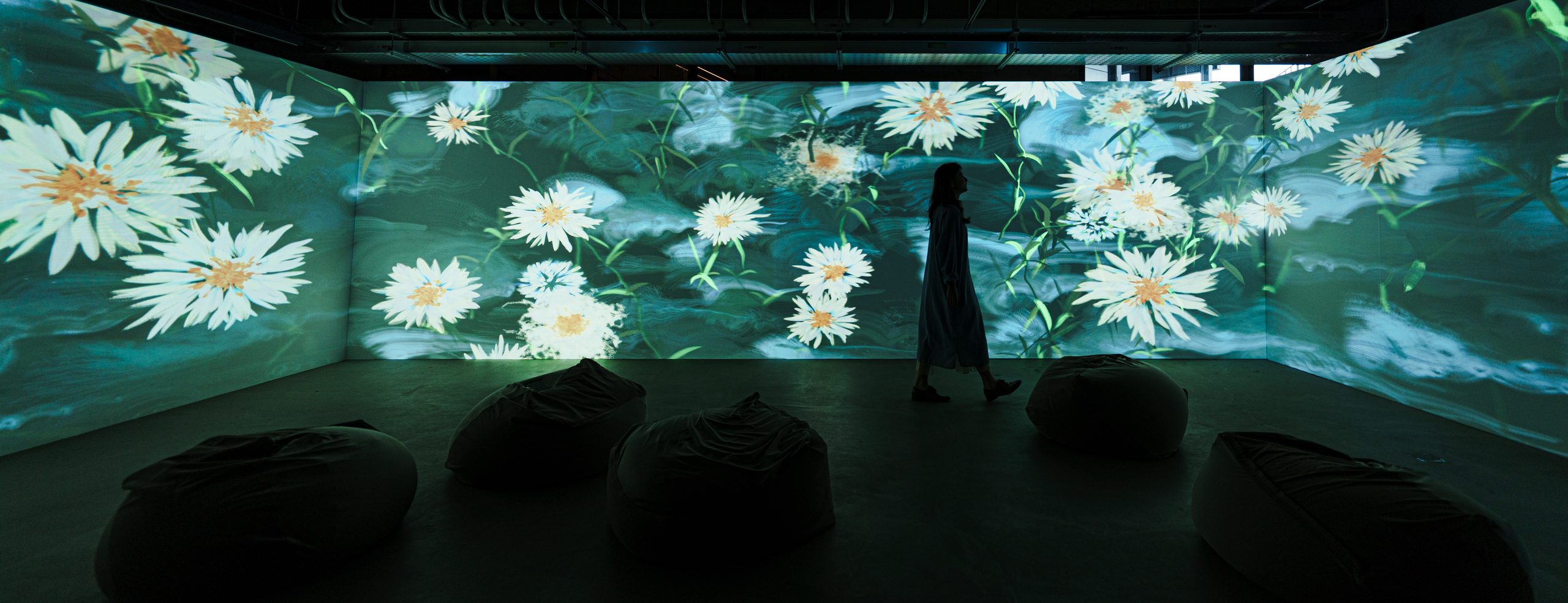 White daisies across the three walls, a visitor walking past the flowers, beanbags on the floor. Photograph by Chao-Ming Huang (Lidio)
